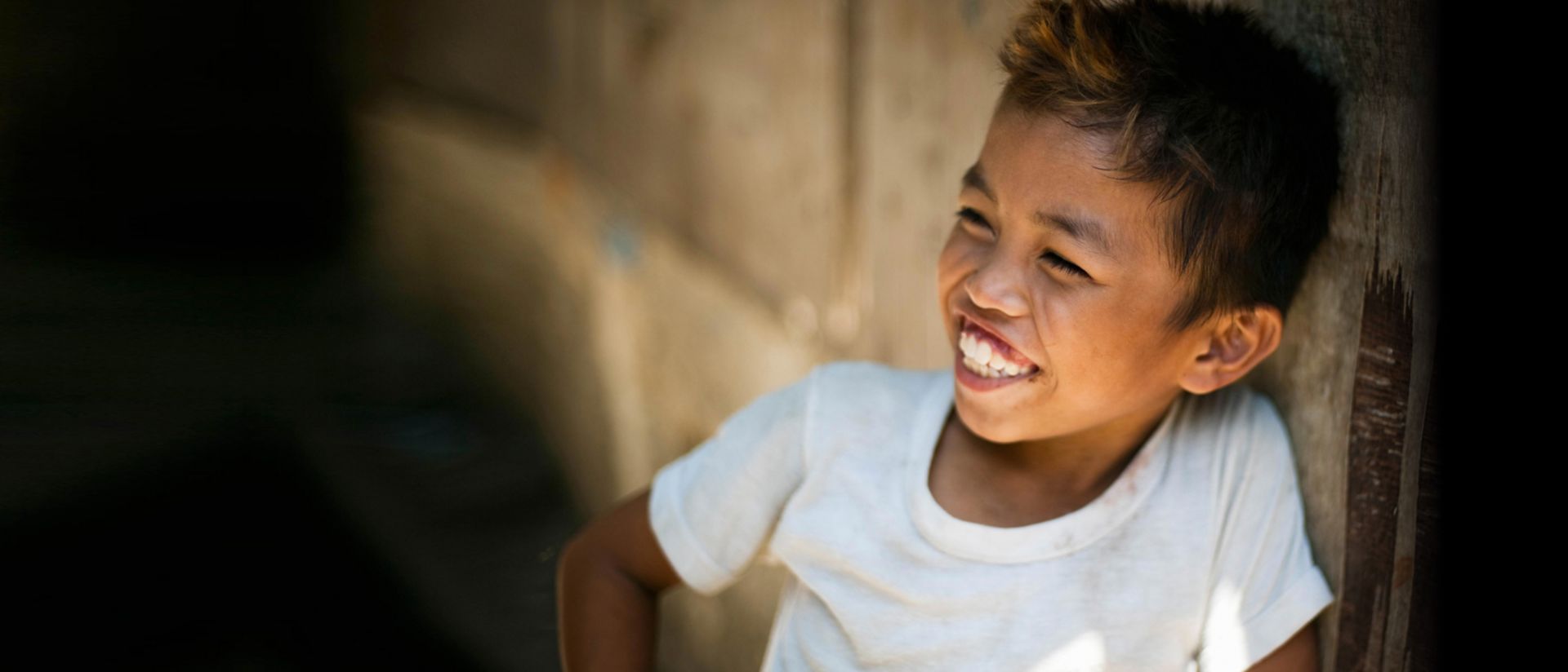uśmiechnięty chłopiec oparty o ścianę stajni