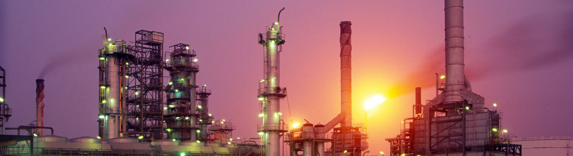 Oil refinery with flames from a flare stack at dusk