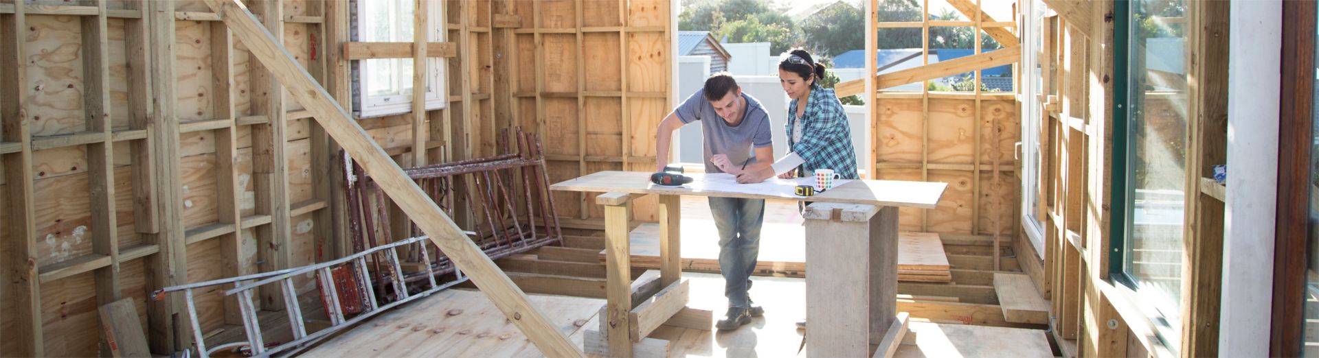 Man and a woman looking at some plans while building a wooden house