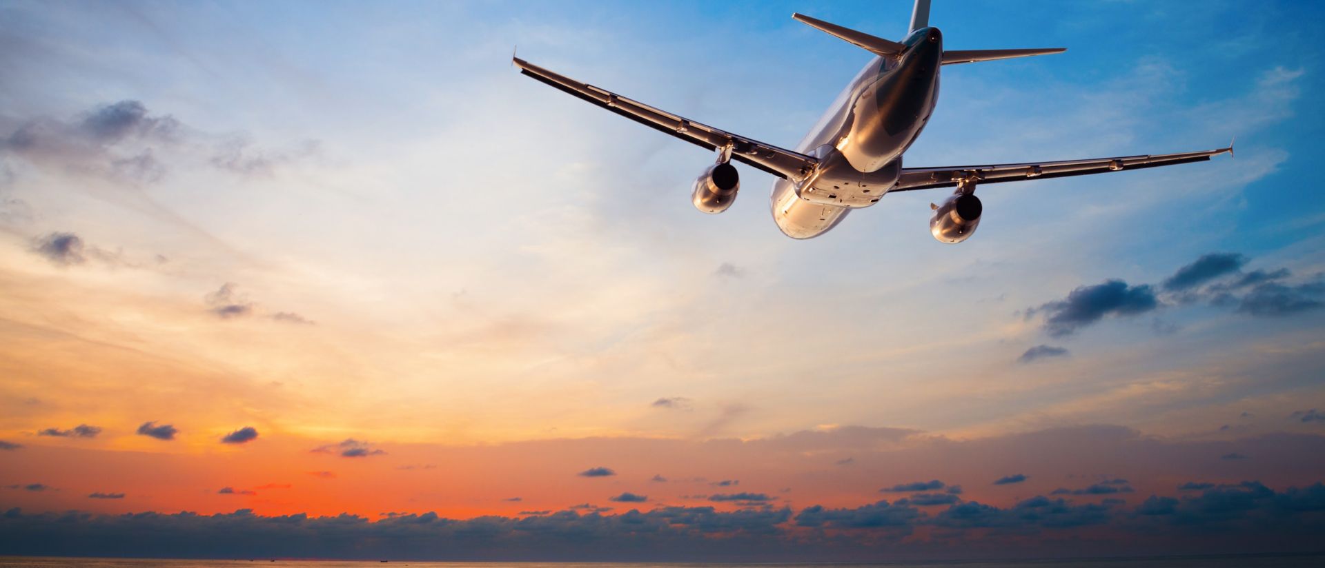 Image of an airplane flying above tropical sea at sunset