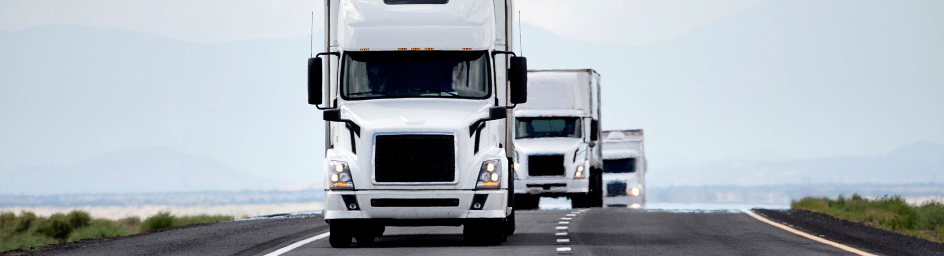 Three oncoming semi-trailer trucks driving on a two-lane road