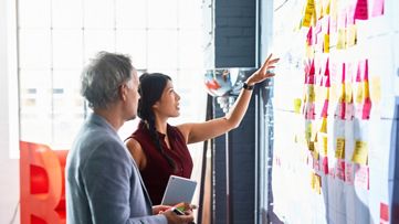 Två kollegor som tittar på klisterlappar på väggen