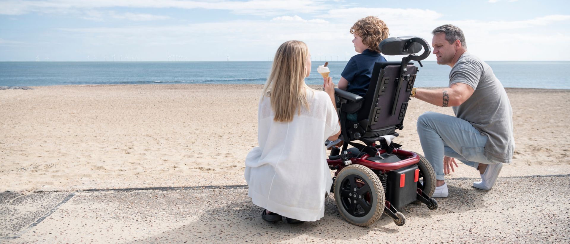 Parents crouching by son in wheelchair at beach