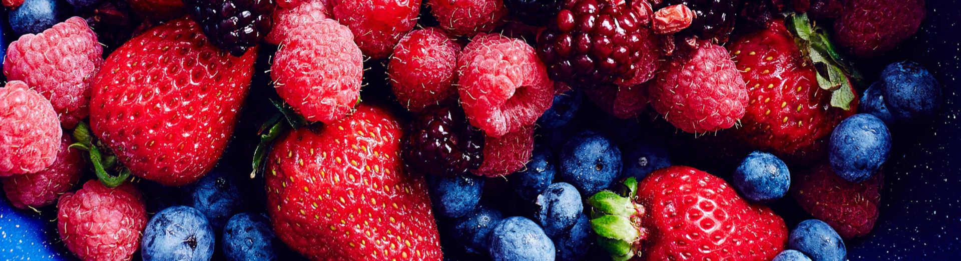 Image of a grocery store display of an abundance of strawberries, blackberries, blueberries, raspberries, and cranberries
