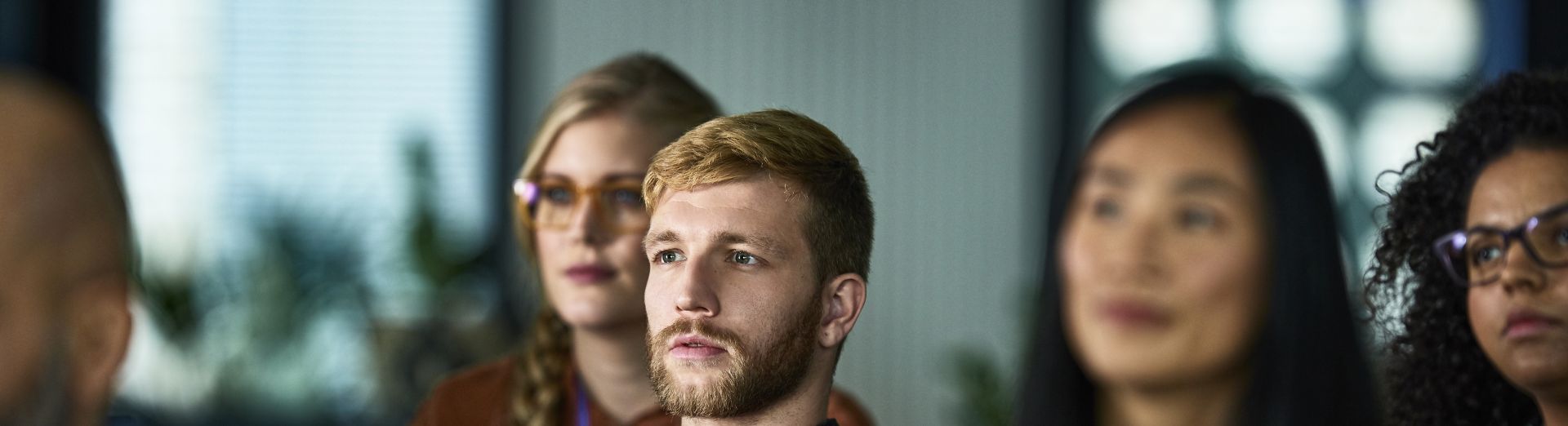 Publikum sidder til konference og lytter, hvor en mand er i fokus med en tablet i hånden
