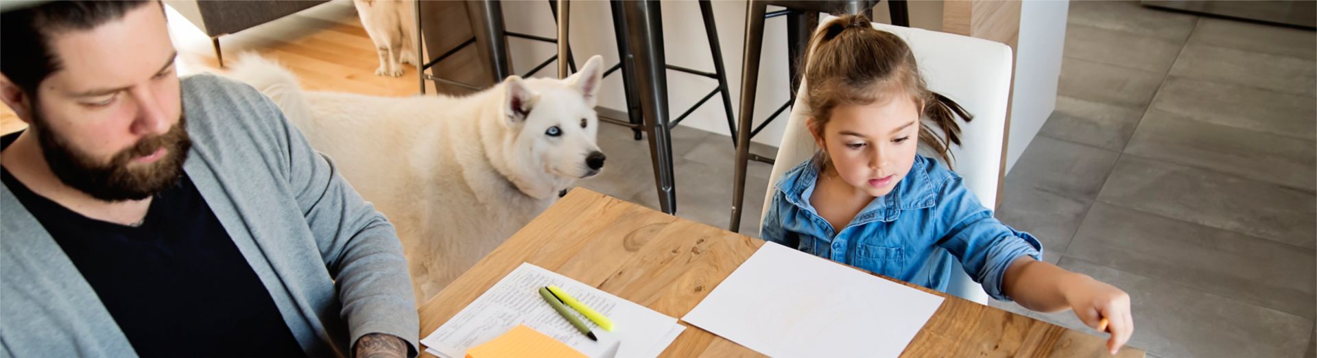 Photo of a father working at the kitchen table while his two children draw pictures