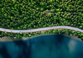 drone photo of a road that goes through the forest next to a lake