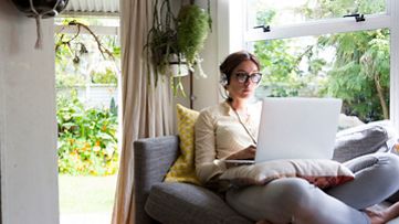 Eine Frau trägt einen Kopfhörer und sitzt auf dem Sofa. Sie verfolgt auf dem Laptop eine Schulung in SAP Learning Hub.