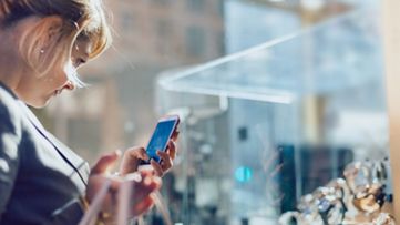 Woman using smart phone making pictures from a shopping window.