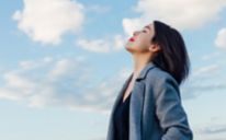 A young women in a blue blazer and black shirt looking up at a sky with clouds
