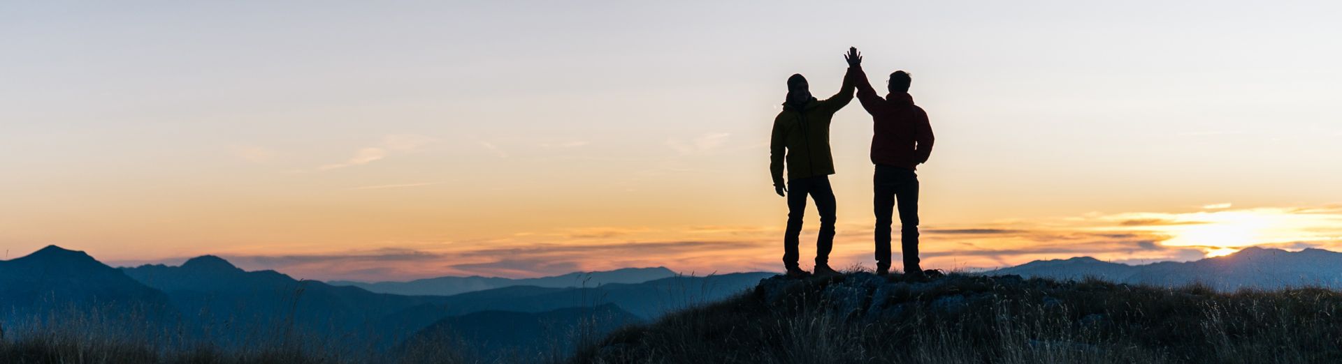 Två personer som står på toppen av ett berg och ser ut över en soluppgång. 