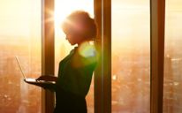 Femeie de afaceri pe laptop la fereastră în soarele dimineții