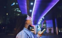 Mladá ázijská žena používajúca mobilný telefón pri státí pod mostom pre chodcov