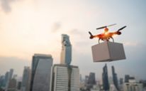 An image of a drown holding a box, flying above a city skyline.