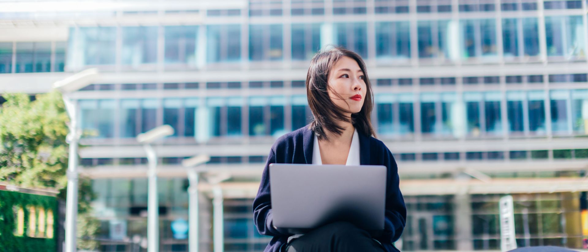 Afbeelding van een vrouw die voor een gebouw achter een laptop zit