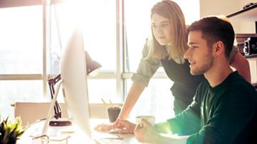 Two coworkers looking at a computer monitor together