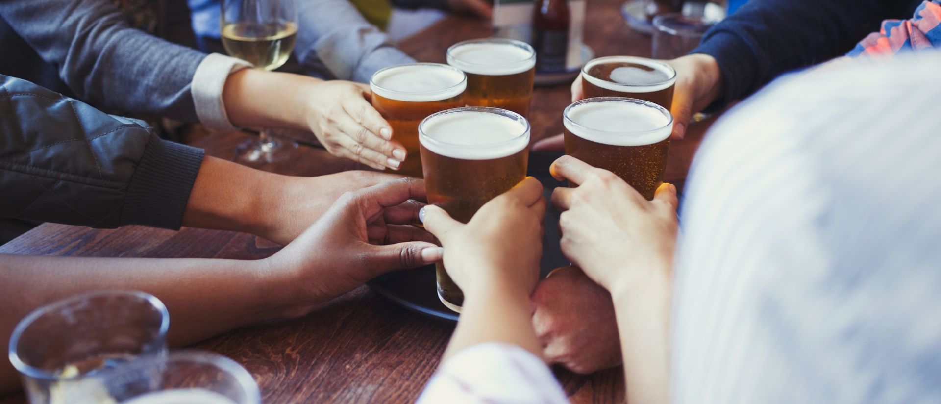 Friends reaching for beer glasses on bar table