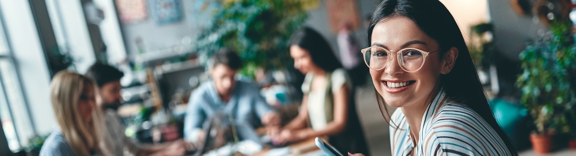 Akıllı telefon kullanan müşteri hizmetleri çalışanı ve arka planda çalışan iş arkadaşları