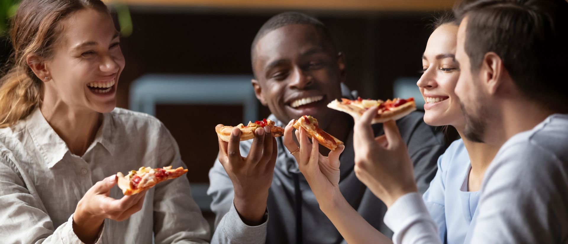 Cheerful multiracial happy friends laugh share pizza in cafe together