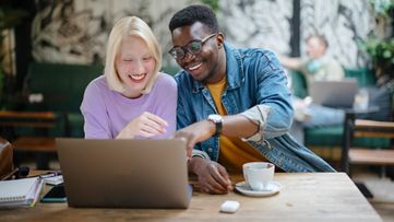 Two people look at a laptop while smiling at a cafe