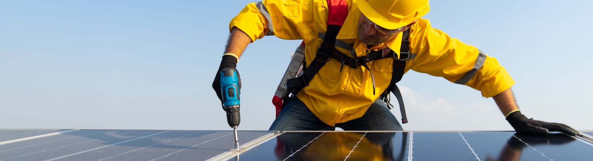 A worker with a hard hat and safety gear installing solar panels