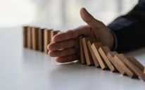 A line of wooden dominos set up in a row with a hand stopping half the dominoes from falling.