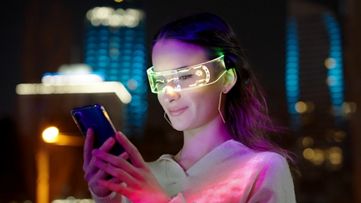 Femeie cu ochelari într-un laborator care se uită la un telefon