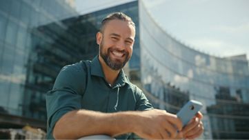 גבר יושב מחייך ומסתכל בטלפון שלו.