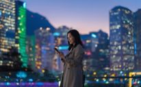 Image of a woman holding her phone with a city skyline in the background