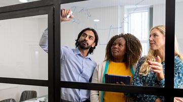 Three colleagues standing at a whiteboard, writing and talking.