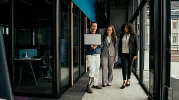 Three colleagues standing in the hallway of an office building, engaged in conversation