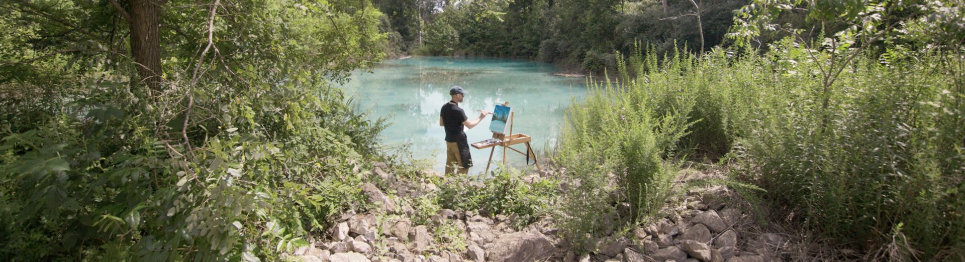 Artist paints on a canvas in front of a river